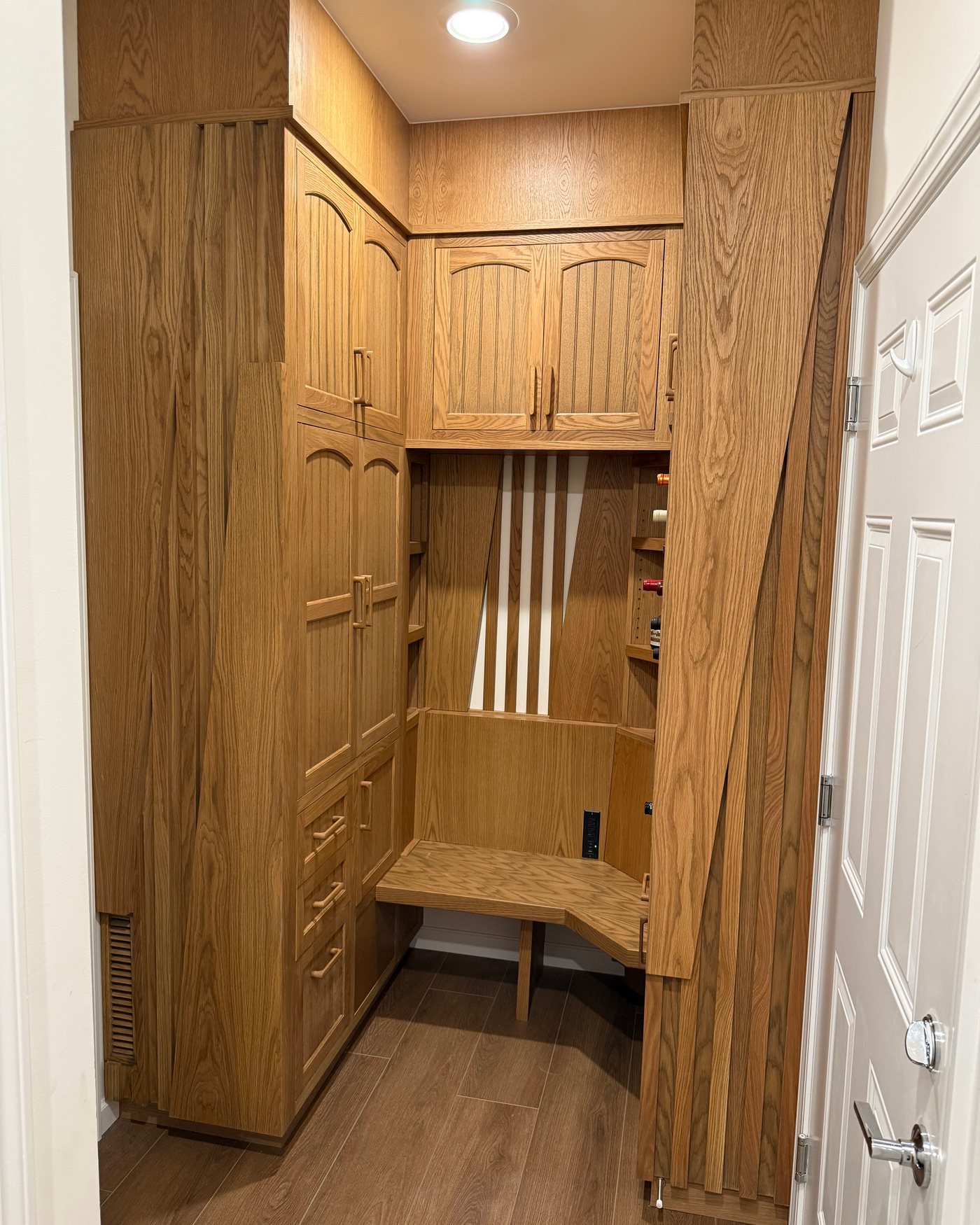 A custom built-in corner unit in white oak, with arched beadboard cabinet doors, a corner bench and drawers